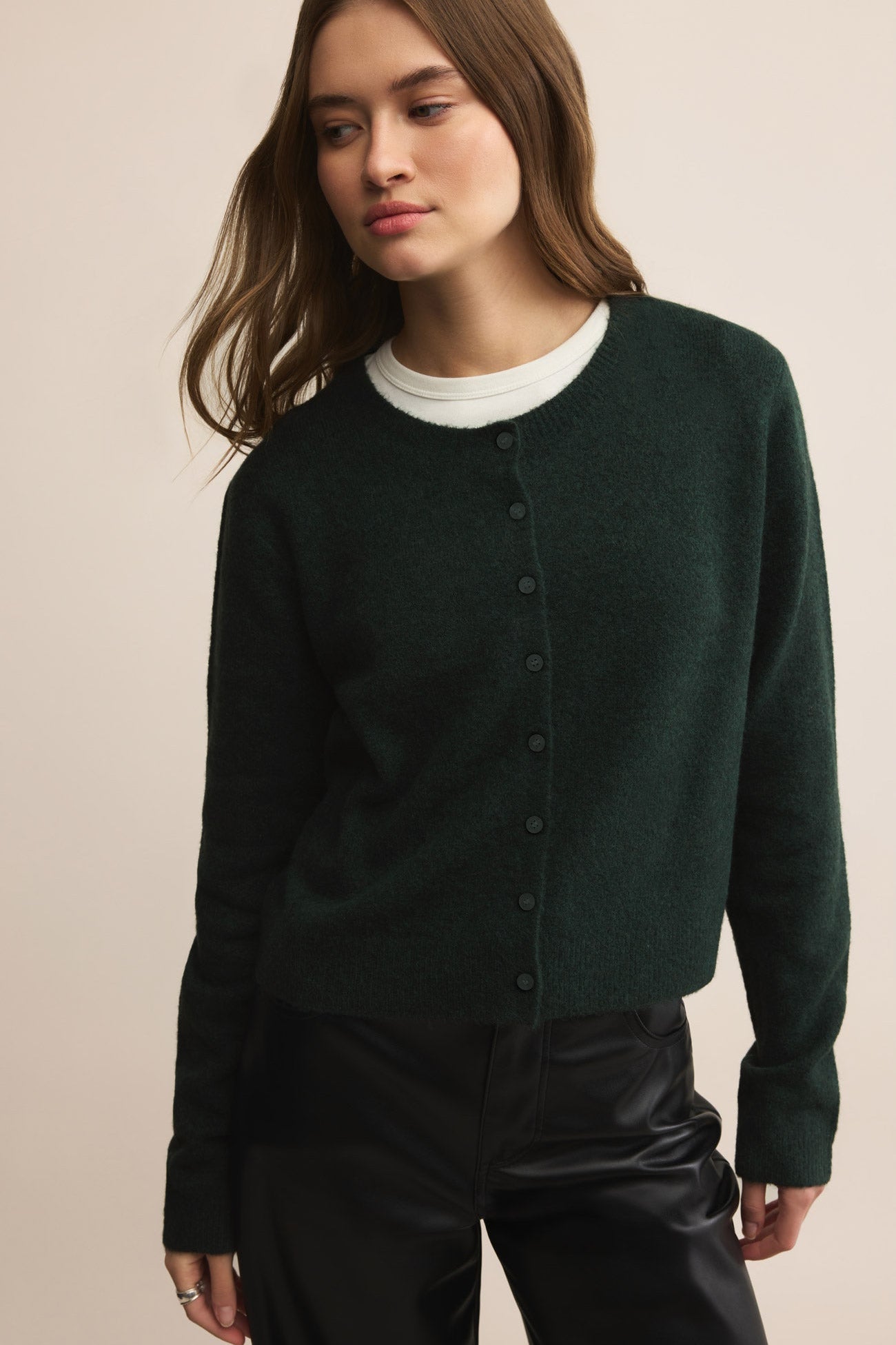 Woman wearing a dark green cardigan over a white shirt on a beige background