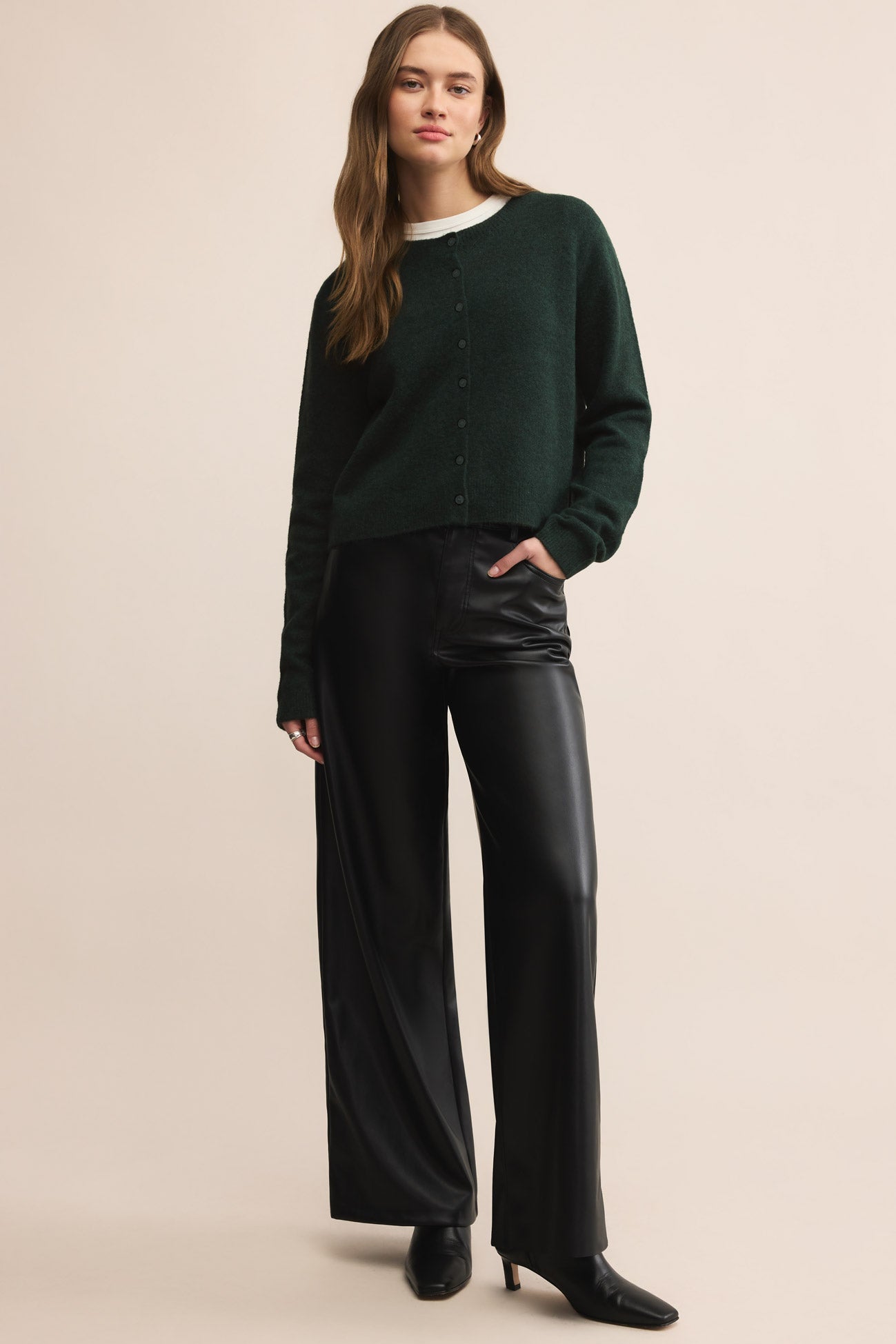 Woman wearing a dark green sweater and black pants on a beige background