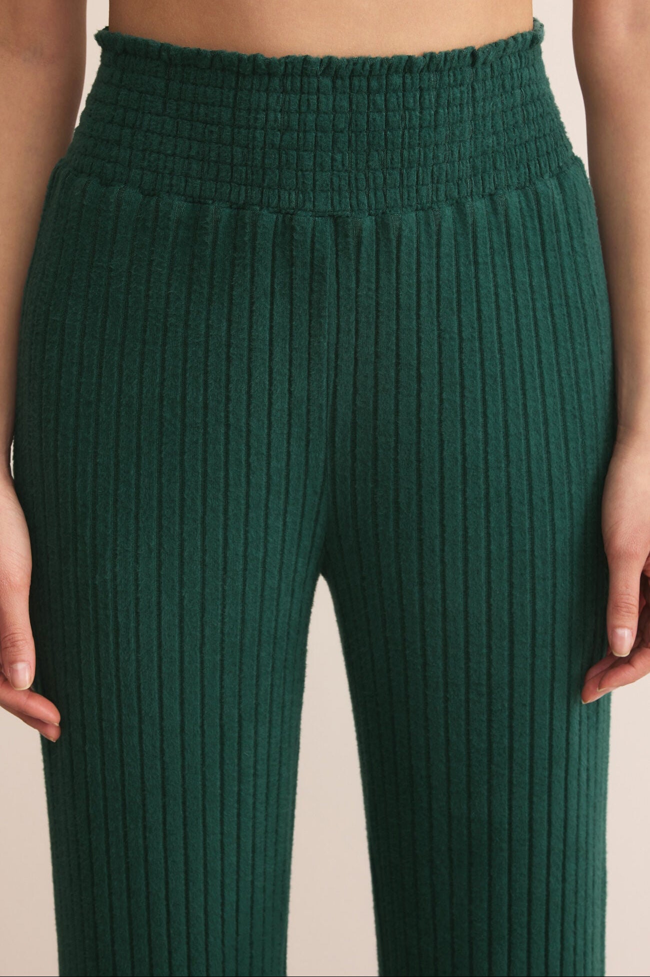 Green ribbed pants worn by a person on a beige background