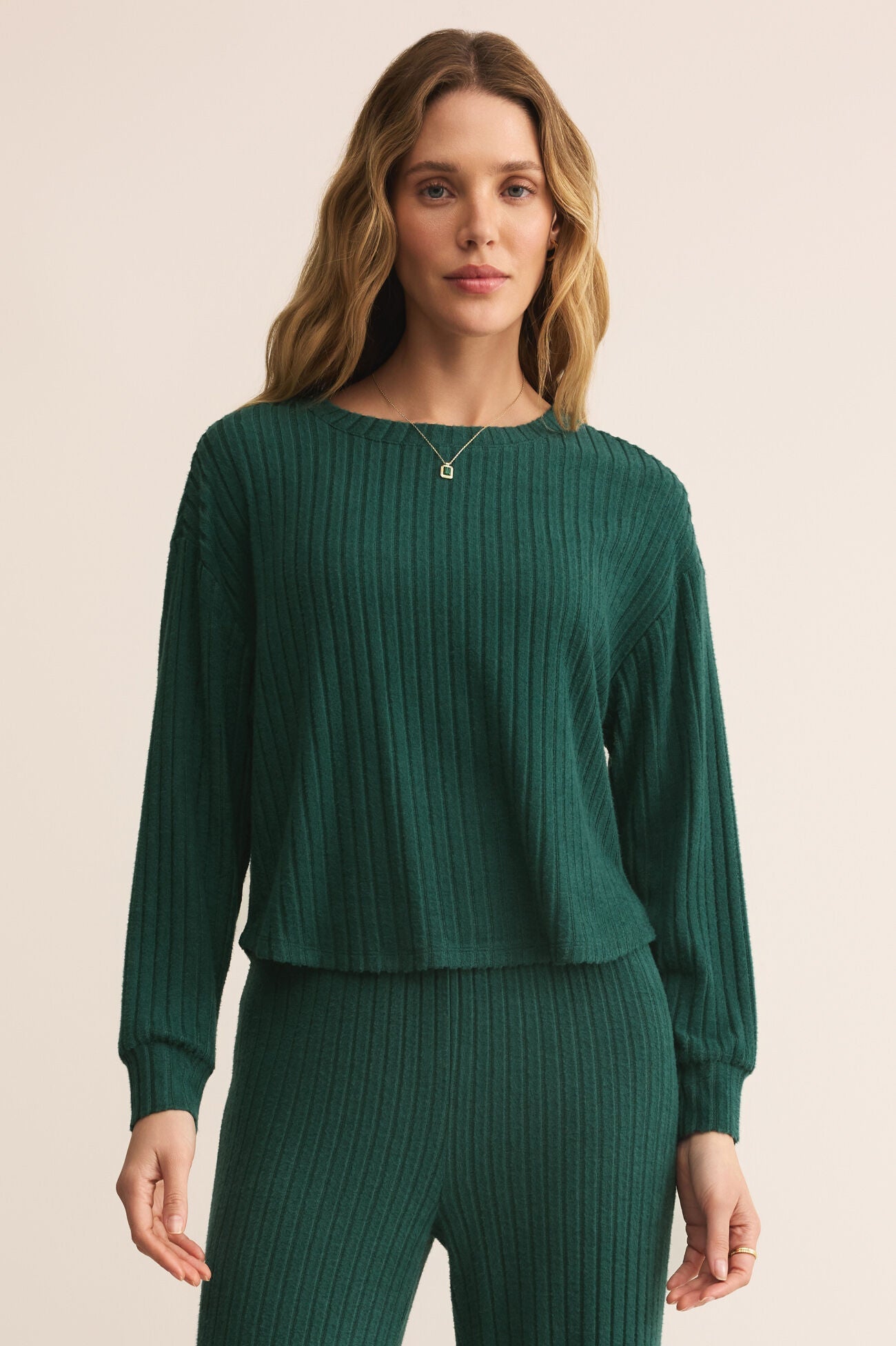 Woman wearing a green ribbed sweater and pants on a beige background