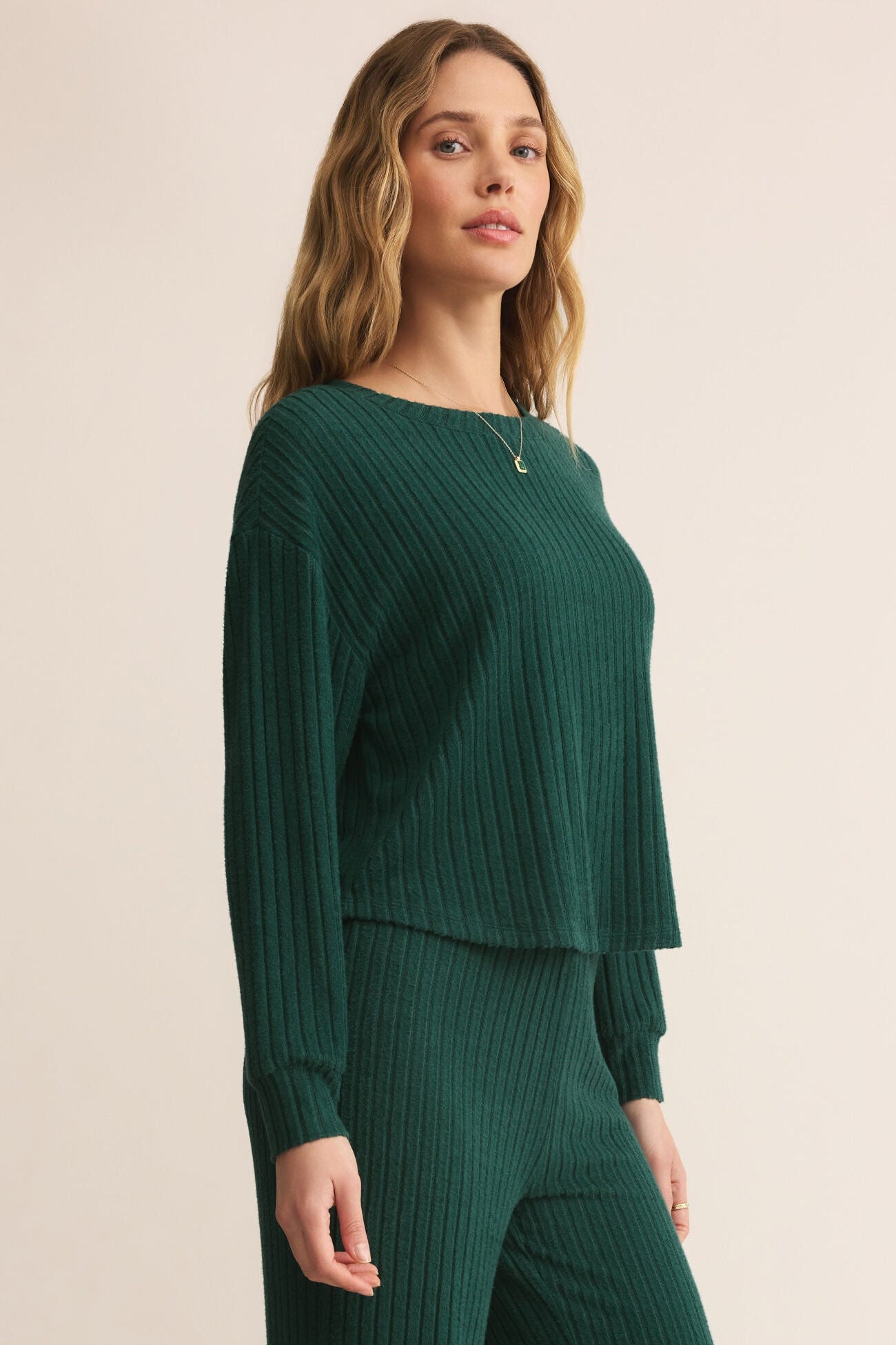 Woman wearing a green ribbed sweater and pants on a beige background
