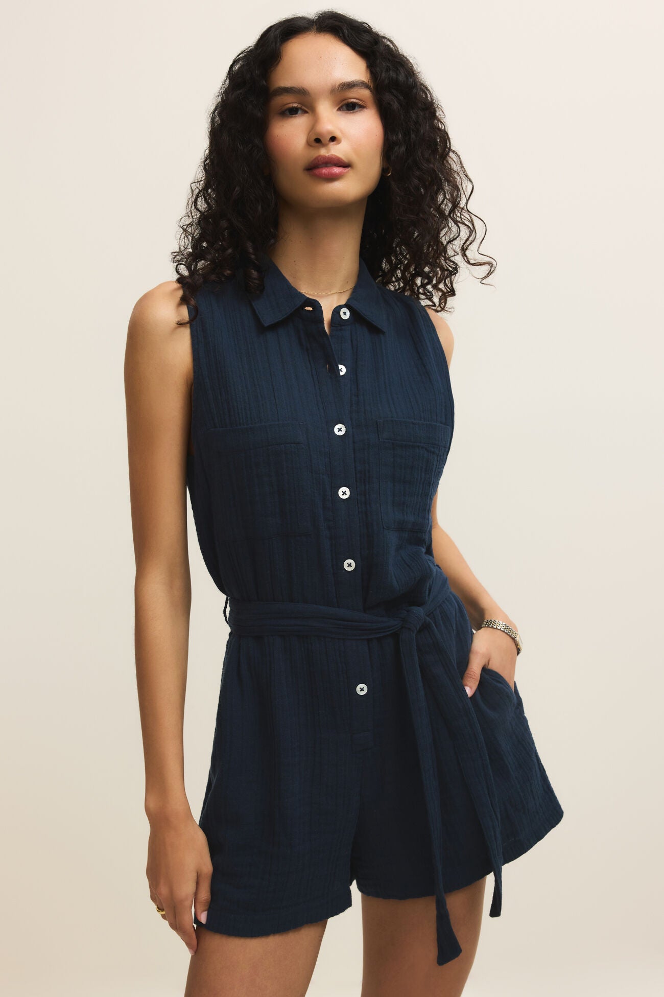 Woman wearing a navy sleeveless shirt dress against a beige background