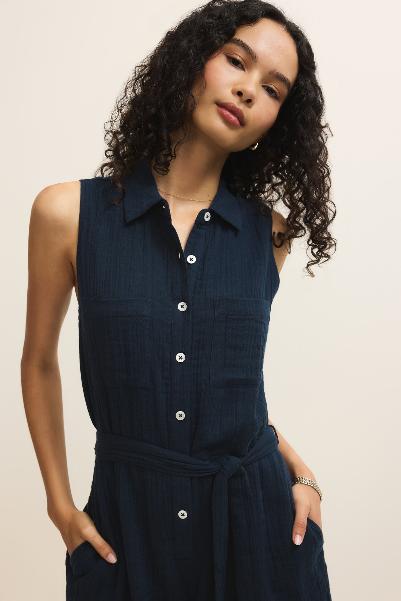 Woman wearing a navy sleeveless dress with buttons on a beige background