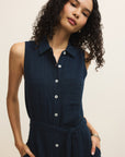 Woman wearing a navy sleeveless dress with buttons on a beige background
