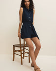 Woman wearing a navy dress standing next to a wooden chair on a beige background