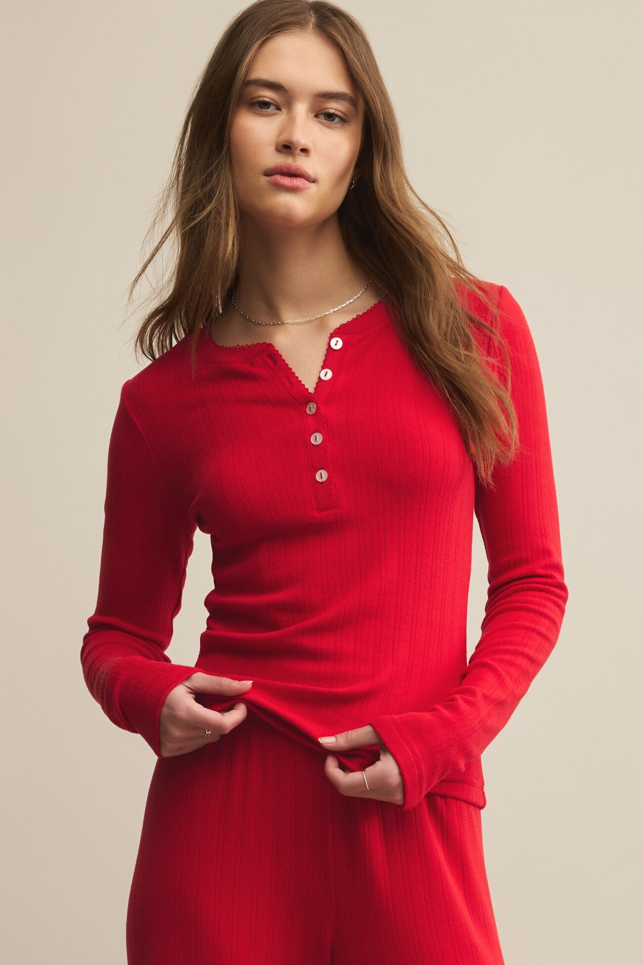 Woman wearing a red long-sleeve top with buttons on a beige background