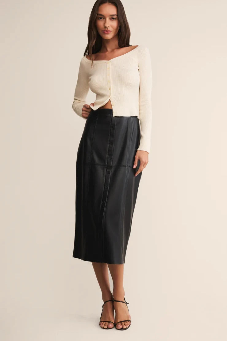 Woman wearing a white off-shoulder top and black leather skirt on a beige background