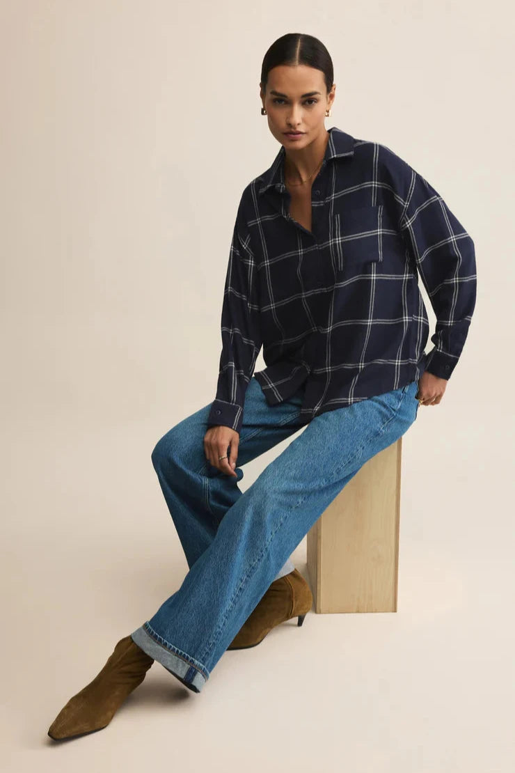 Woman wearing a plaid shirt and blue jeans sitting on a wooden block against a beige background