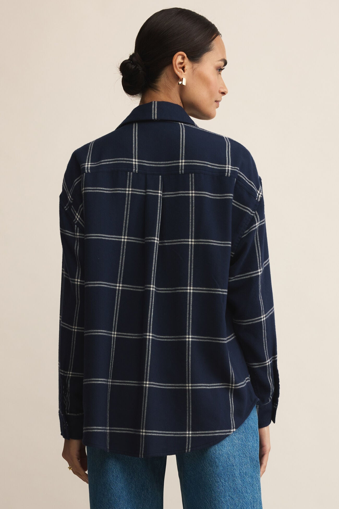 Woman wearing a navy plaid shirt and blue jeans on a beige background