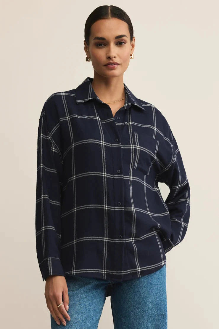 Woman wearing a navy plaid shirt and blue jeans on a beige background