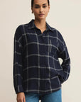 Woman wearing a navy plaid shirt and blue jeans on a beige background