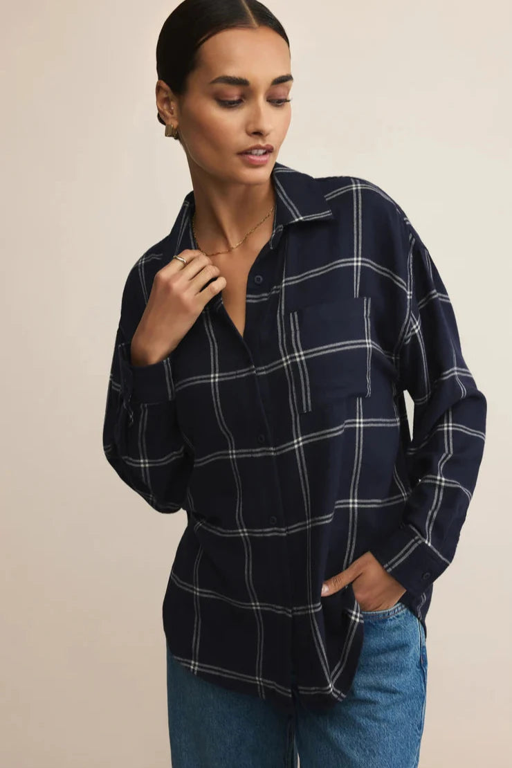 Woman wearing a navy plaid shirt and blue jeans against a beige background