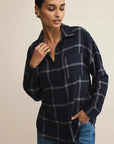 Woman wearing a navy plaid shirt and blue jeans against a beige background