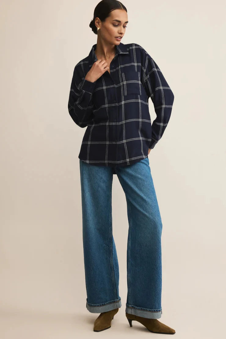 Woman wearing a navy plaid shirt and blue jeans on a beige background