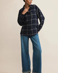 Woman wearing a navy plaid shirt and blue jeans on a beige background