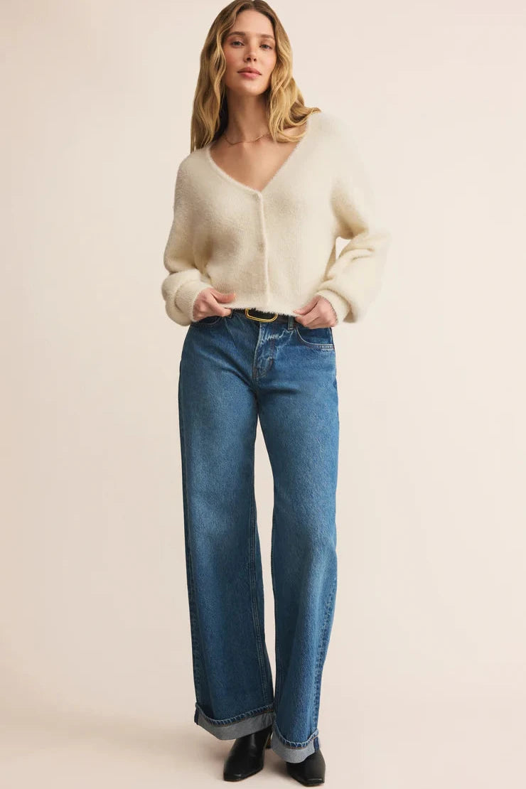 Woman wearing a cream cardigan and blue jeans on a beige background