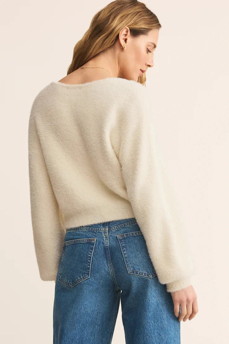 Woman wearing a cream sweater and blue jeans on a beige background