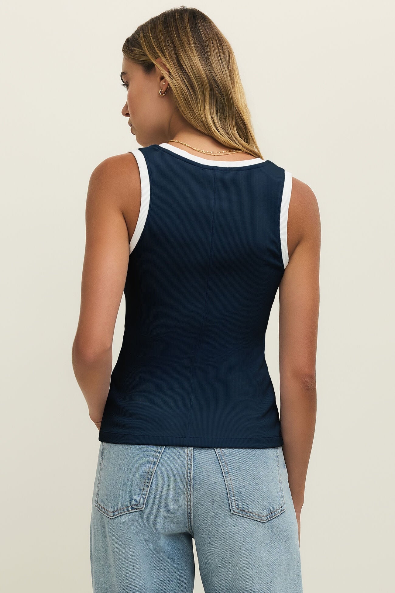 Person wearing a navy tank top with white trim and light blue jeans on a beige background