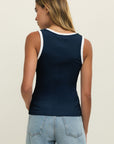Person wearing a navy tank top with white trim and light blue jeans on a beige background