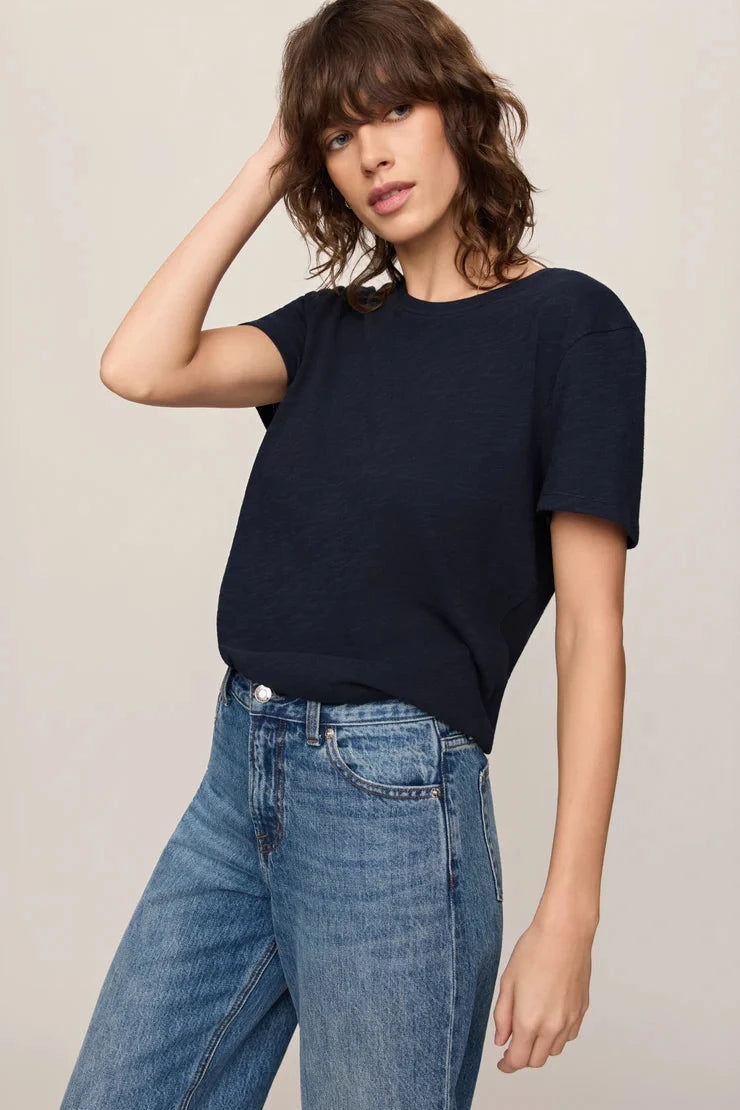 Woman wearing a navy blue sweater and blue jeans against a beige background