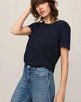 Woman wearing a navy blue sweater and blue jeans against a beige background