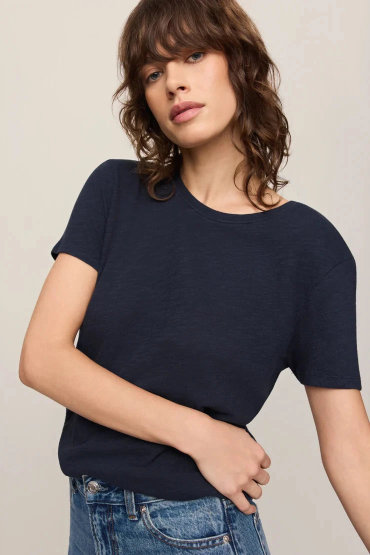 Woman wearing a navy blue t-shirt and blue jeans against a plain background