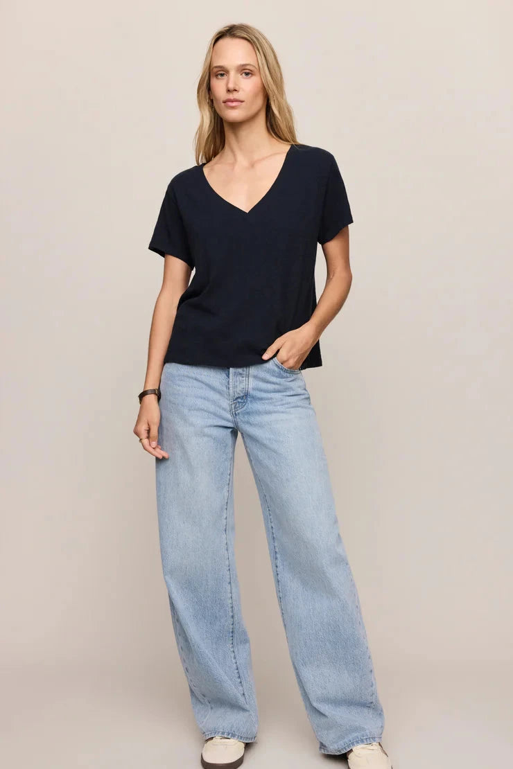 Woman wearing a black V-neck top and light blue jeans on a plain background
