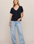 Woman wearing a black V-neck top and light blue jeans on a plain background