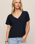 Woman wearing a black V-neck t-shirt and light blue jeans on a beige background