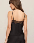 A woman shown from the back wearing a black satin camisole-style top with thin straps and a lace band across the upper back, against a plain light beige studio background.