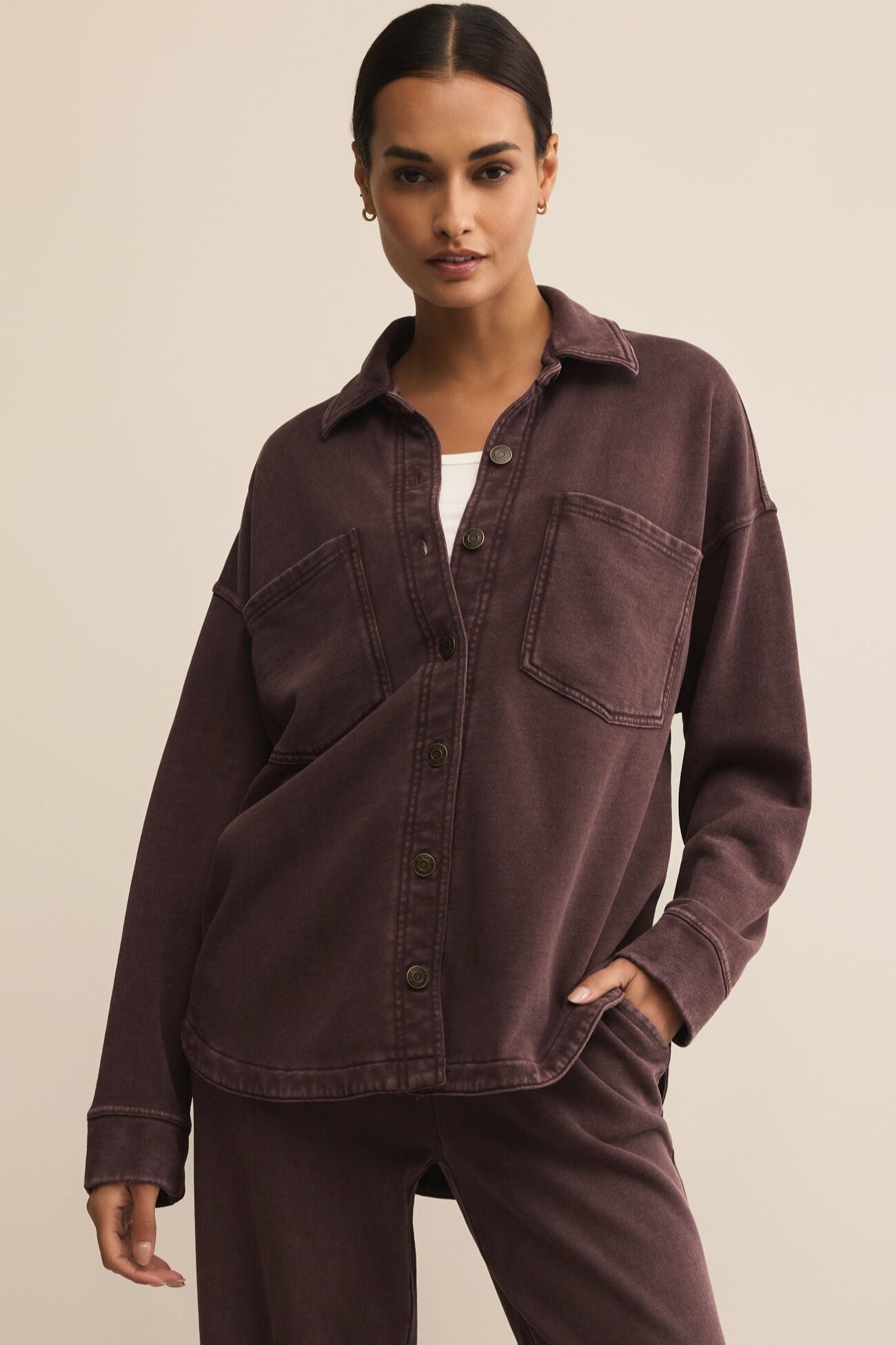 Woman wearing a brown shirt and pants against a beige background