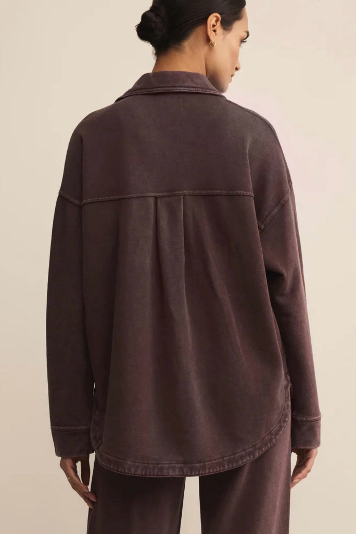 Person wearing a brown jacket and pants on a beige background
