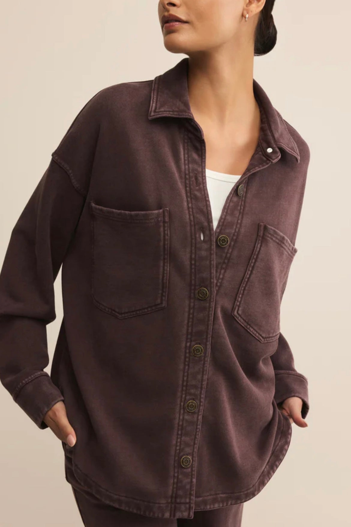 Person wearing a dark brown button-up shirt with pockets on a beige background
