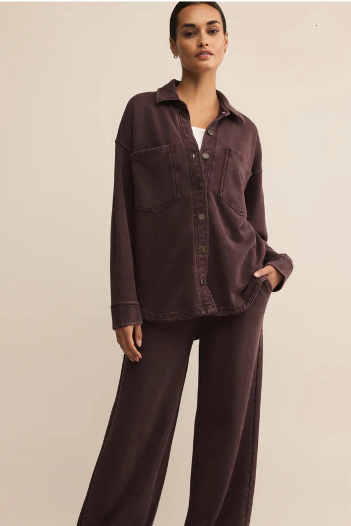 Woman wearing a brown shirt and pants against a beige background