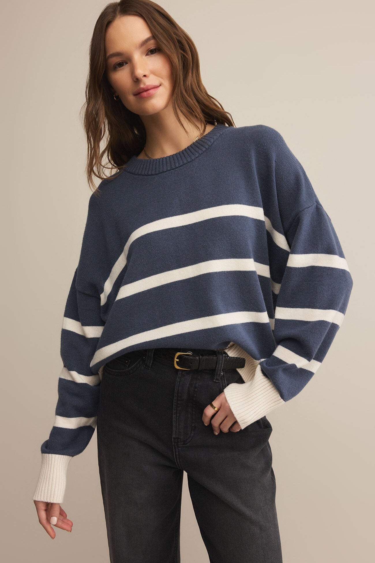Woman wearing a blue and white striped sweater with black pants on a beige background