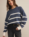 Woman wearing a blue and white striped sweater with black pants on a beige background