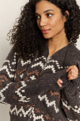 Woman wearing a dark gray sweater with a pattern, against a neutral background