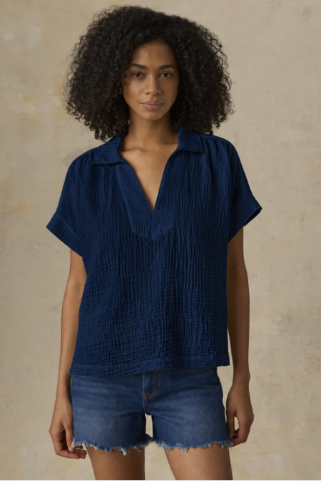 Woman wearing a blue textured blouse and denim shorts against a beige background