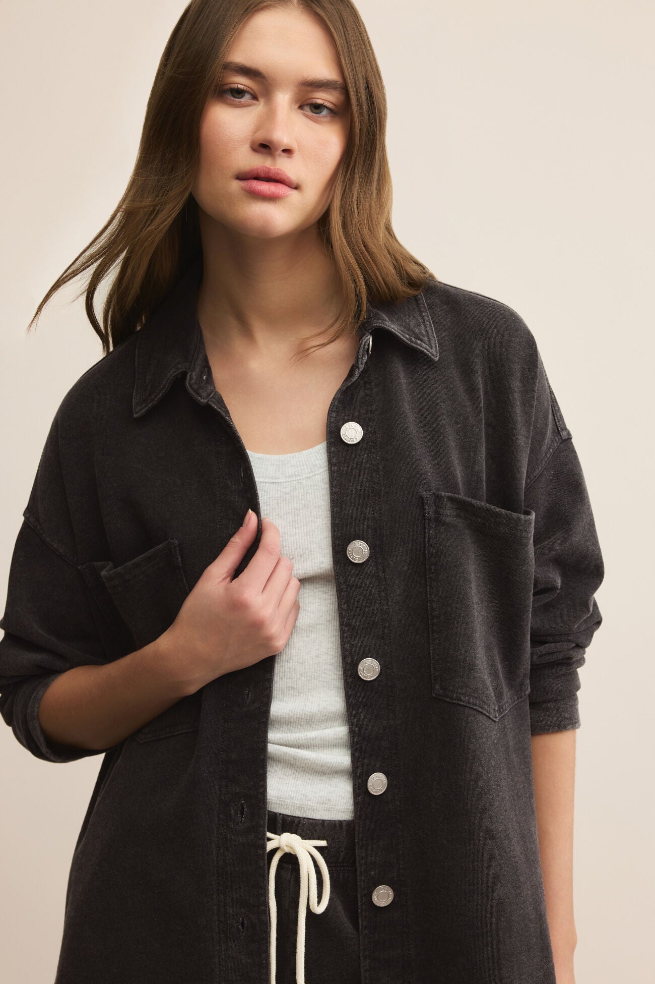 Woman wearing a black button-up shirt over a white top on a beige background