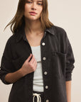 Woman wearing a black button-up shirt over a white top on a beige background