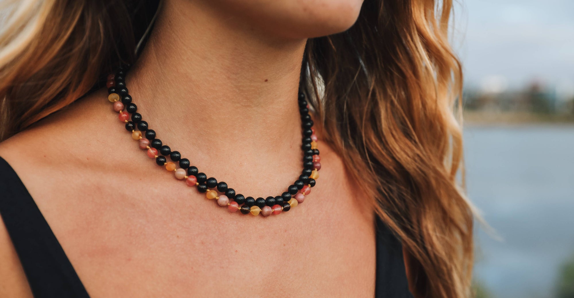 Close-up of a woman wearing a beaded necklace with a blurred natural background