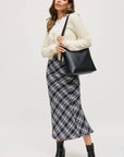 Woman holding a black handbag wearing a plaid skirt and white sweater on a white background
