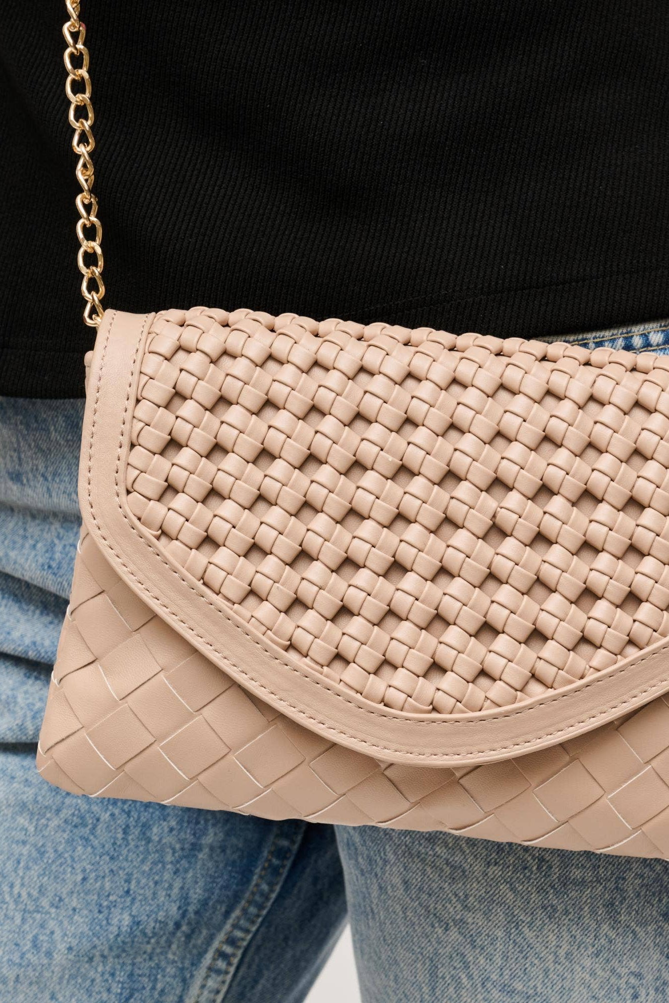 Beige woven handbag worn over the shoulder with a person wearing a black top and blue jeans.