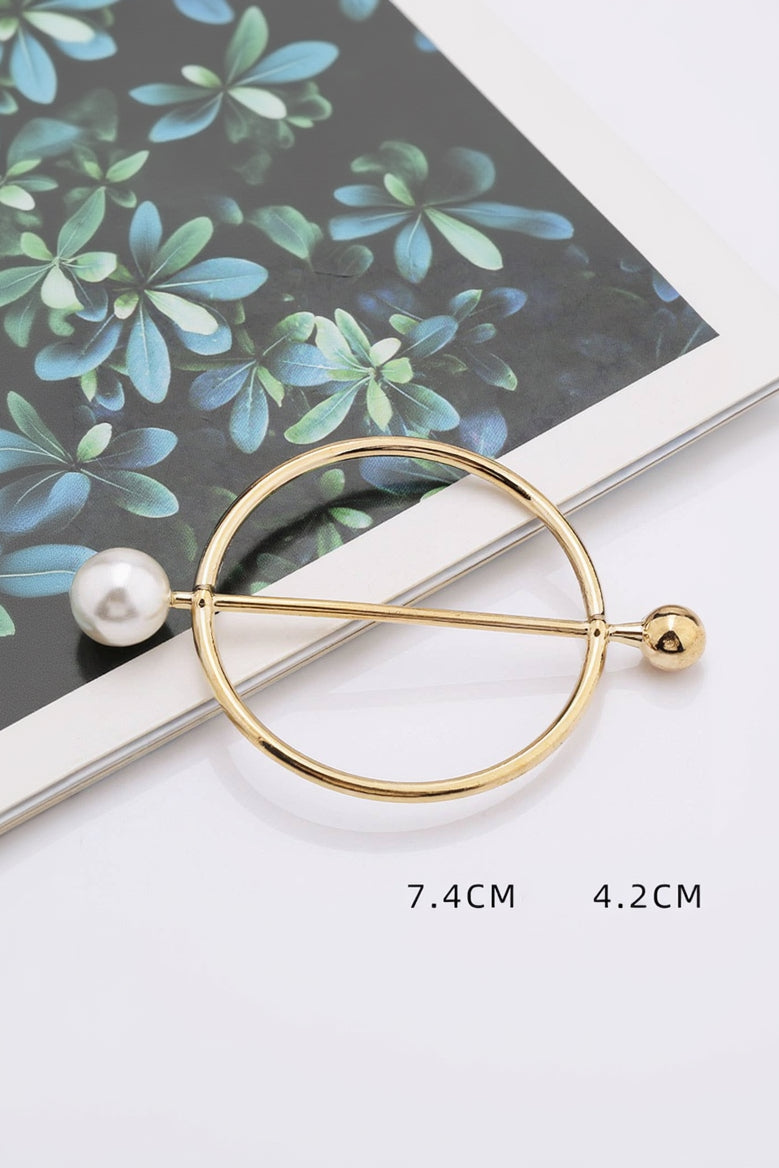 Gold brooch with pearls on a white surface with green leaves in the background