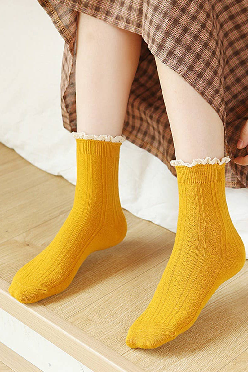 Person wearing yellow socks with lace trim on a wooden floor.