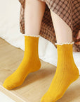 Person wearing yellow socks with lace trim on a wooden floor.