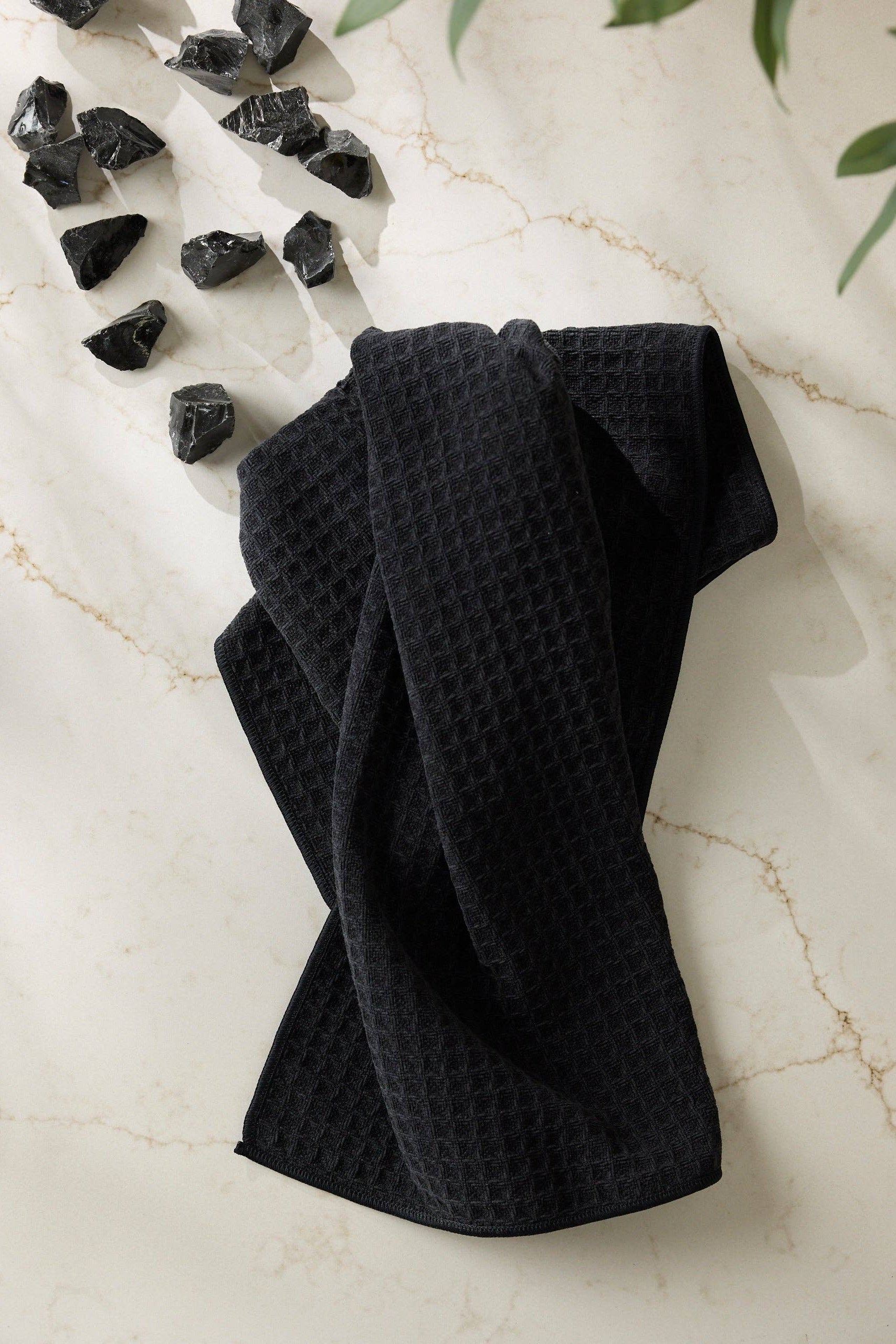 Black waffle-textured towel on a marble surface with black stones and green leaves.