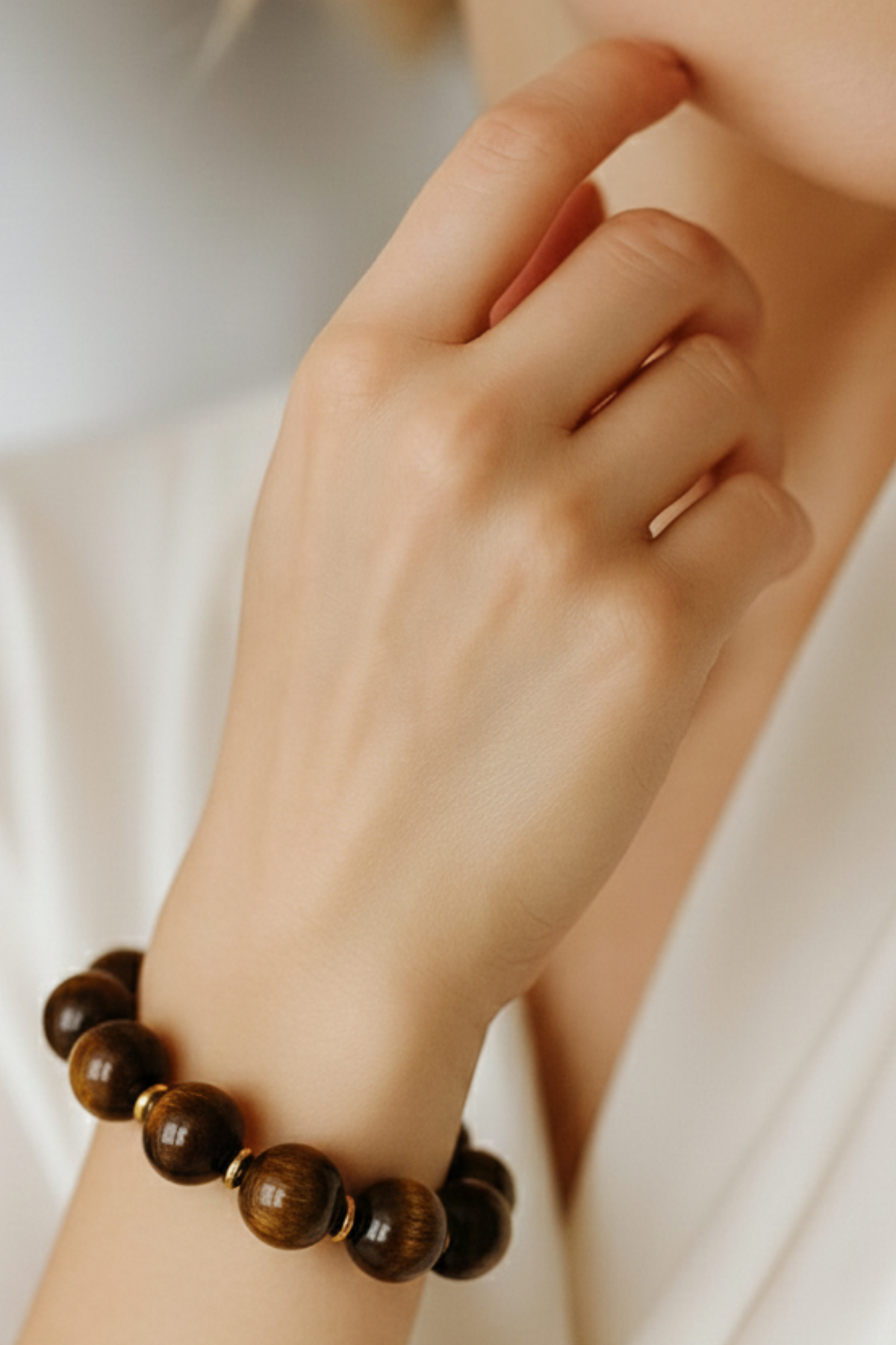 Close-up of a hand wearing a brown beaded bracelet on a white background