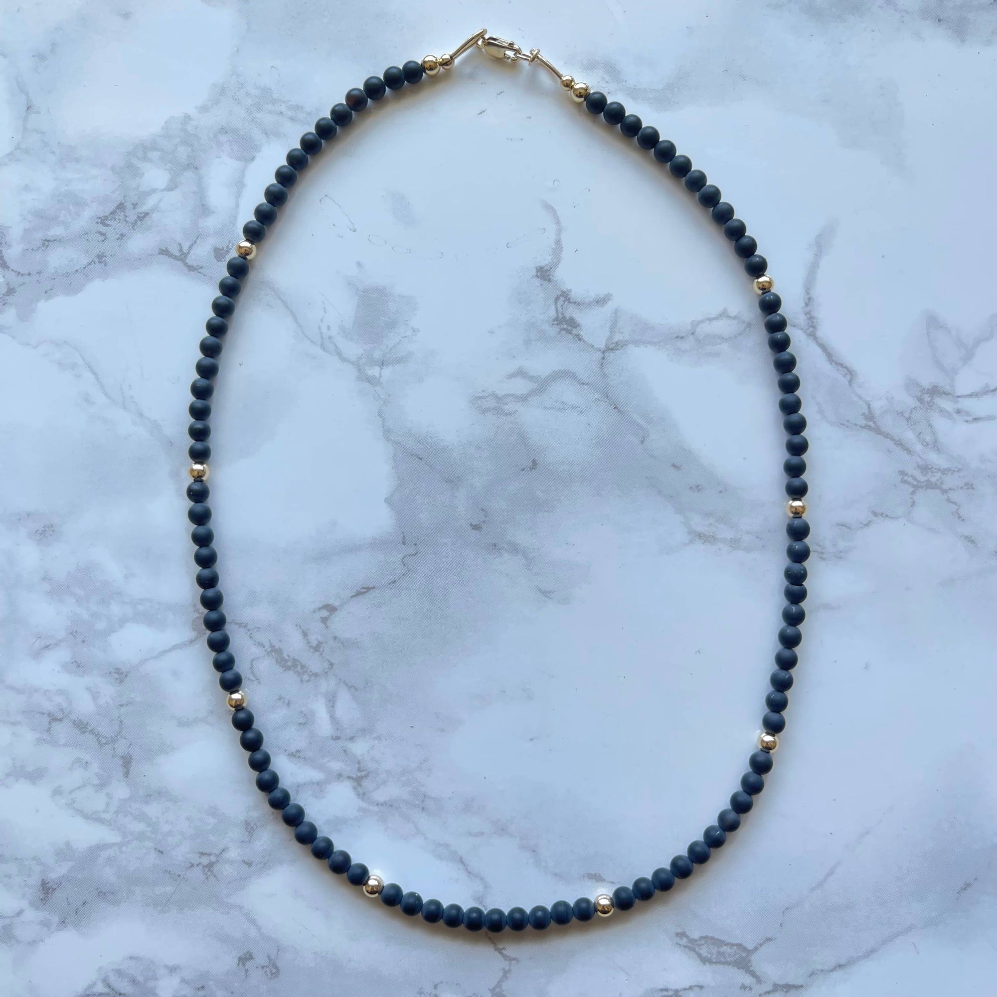 Necklace with dark blue beads and gold accents on a marble surface