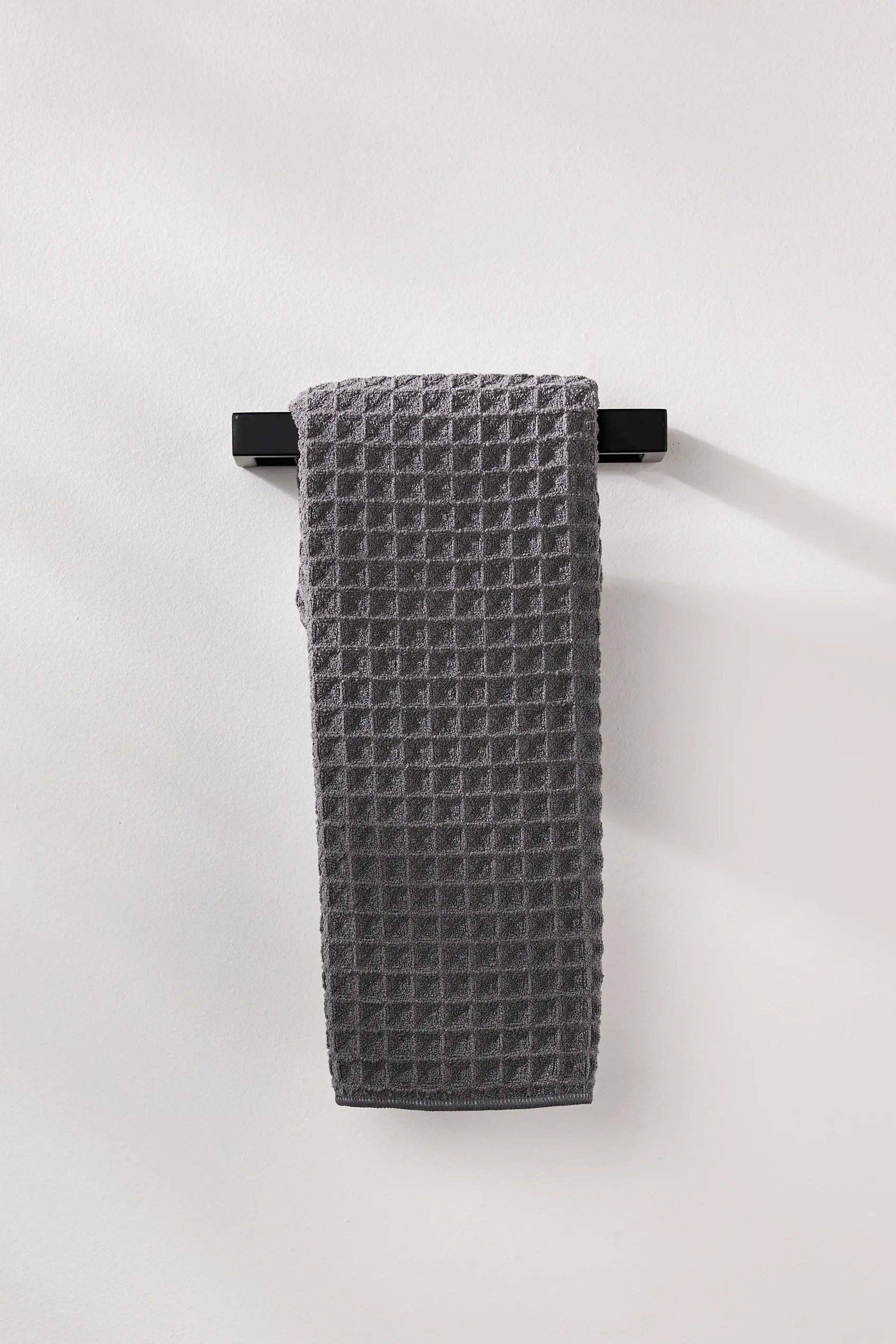 Gray textured towel hanging on a black rack against a white background